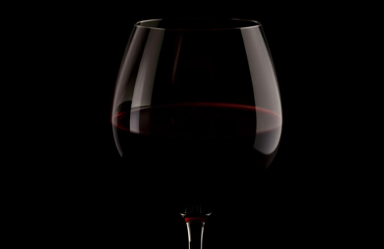 A deep opaque red wine in a large Bordeaux glass under moody warm low light.